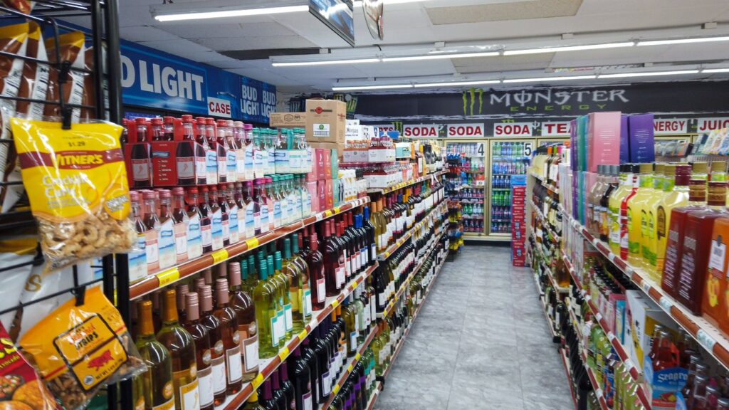 A welcoming, well-lit aisle displays a wide selection of wines and liquors; coolers in back offer Bud Light, soda, and energy drinks.