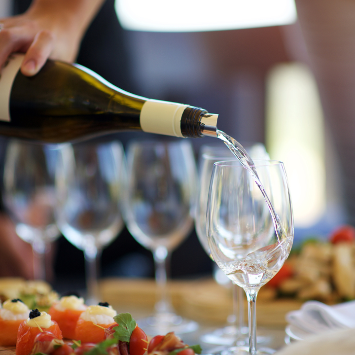 A bottle of white wine being poured into a glass at a beautifully set table with appetizers and elegant glassware.