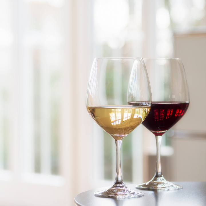 "Two elegant wine glasses filled with red and white wine, placed on a modern table with natural light streaming through large windows in the background."