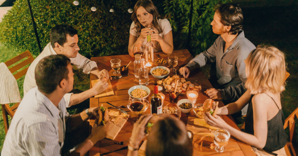 Friends Sharing Dinner and Drinks Outdoors at Night with Wine and Food