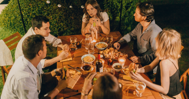Friends Sharing Dinner and Drinks Outdoors at Night with Wine and Food