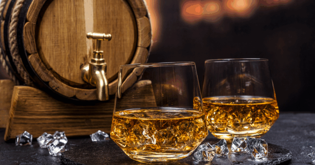 Two Glasses of Whiskey on Ice with a Wooden Barrel in the Background