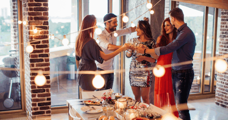 Group of friends toasting with wine and cocktails at a stylish home party with string lights