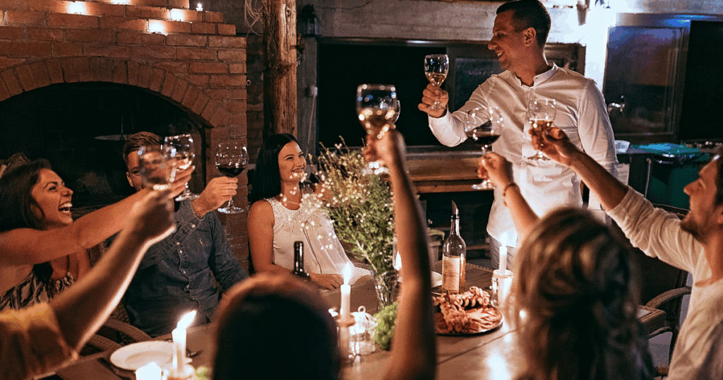 Friends raising wine glasses in a toast at a dinner party with candles and food on the table
