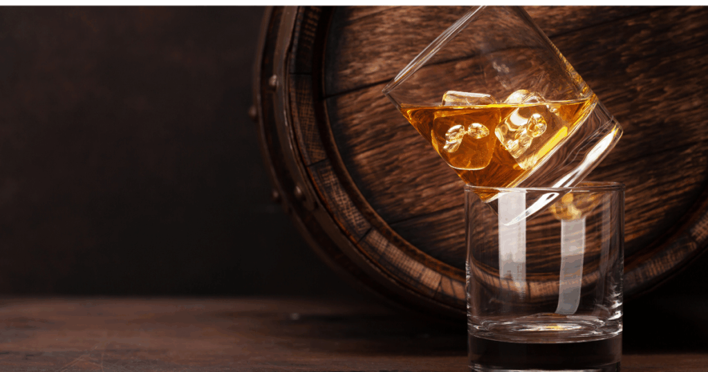 Inner Circle Members Are Grabbing These Bottles First, Here’s What You’re Missing 1 Glass of whiskey on ice being poured over a wooden bourbon barrel, symbolizing rare allocated whiskey for the Inner circle members at Pina Wine and Spirits.