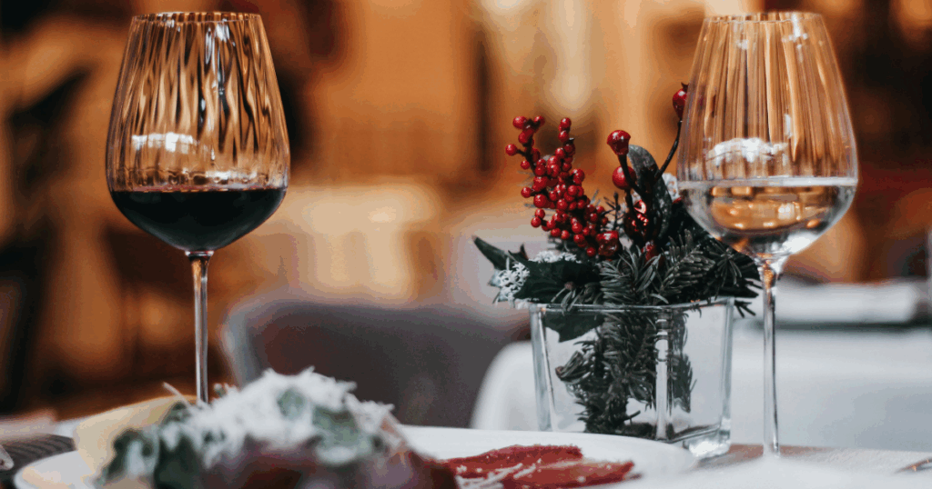 Holiday Hosting Made Easy: Must-Have Wines & Spirits for Christmas Parties in Kansas City 1 Red and white wine glasses on a holiday-themed table with Christmas décor for Kansas City hosting Christmas dinner parties.