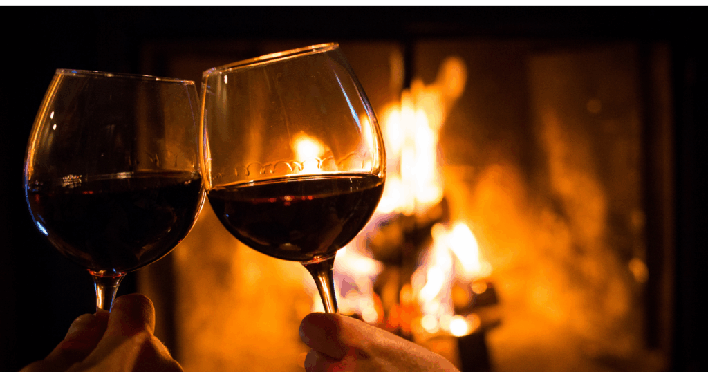 Two glasses of red wine toasting in front of a warm fireplace, representing cozy last-minute dinner party wine pairings.
