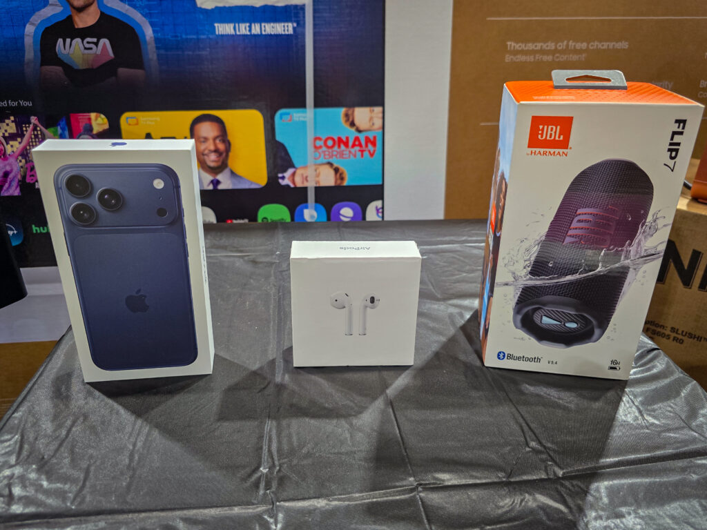 Featured technology raffle prizes including an iPhone, AirPods, and JBL speaker packaging, with a Samsung TV box in the background.